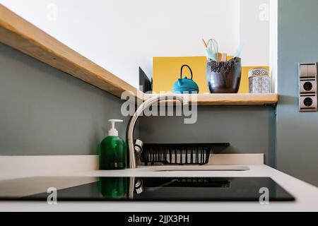 Ferro teiera e ciotola con utensili posti su banco di legno su lavandino con rubinetto cromato e stufa in cucina moderna in luce diurna Foto Stock