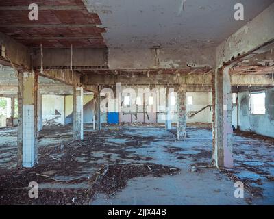 Interno di un edificio industriale desolato scuro con pavimento in shabby e colonne di cemento al tramonto Foto Stock