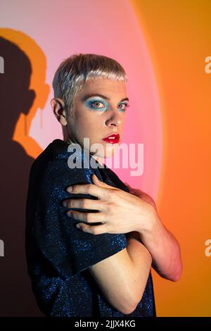 Ritratto di uomo transgender indossando trucco abbracciante in studio illuminato Foto Stock
