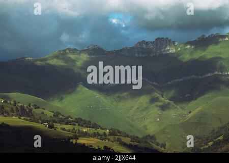 Bellissimo paesaggio naturale di valle verde nel nord della Spagna con alcune case e alberi sparsi intorno alle colline Foto Stock