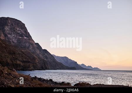 Mare ondinante spiaggia di sabbia con ruvida scogliera rocciosa contro cielo nuvoloso il giorno d'estate nella zona costiera della natura Foto Stock