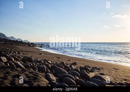 Mare ondinante spiaggia di sabbia con ruvida scogliera rocciosa contro cielo nuvoloso il giorno d'estate nella zona costiera della natura Foto Stock