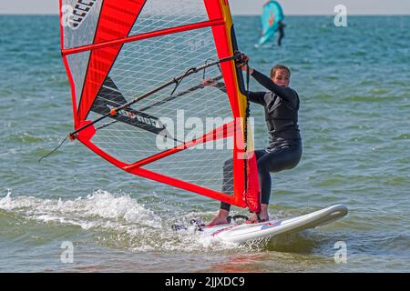 Ragazza / femmina ricreazione windsurf in muta nera praticando il windsurf classico in mare Foto Stock