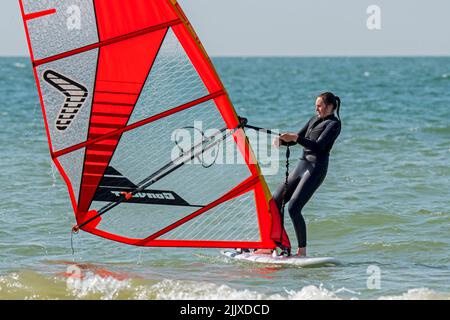Ragazza / femmina ricreazione windsurf in muta nera praticare il windsurf classico e sollevare vela in mare Foto Stock