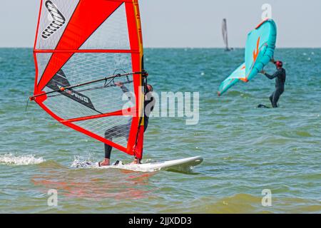 Ragazza / femmina ricreazione windsurfer in muta nera praticando il windsurf classico e wingboarder / ala boarder alare fodere in mare Foto Stock
