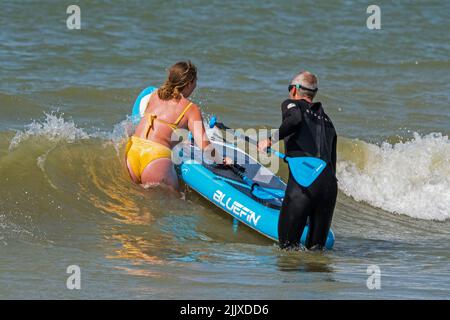 Paddleboarding, due pedalate ricreative che entrano in acqua con paddleboard lungo la costa del Mare del Nord Foto Stock