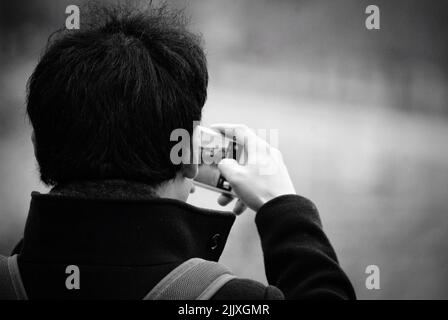 Vista posteriore in scala di grigi ravvicinata di un uomo che scattava una foto con il telefono e con uno sfondo sfocato Foto Stock