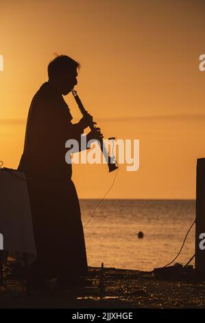 Il musicista in silhouette suona strumenti all'alba sul mare Foto Stock