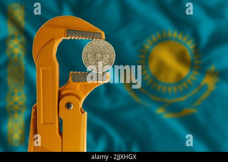 50 Kazakhstani tenge tenuto in una chiave per idraulico arancione sullo sfondo della bandiera del Kazakistan. Emblema del Kazakistan Foto Stock