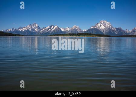 La catena montuosa del Grand Teton National Park viene fotografata durante una mattinata con i riflessi delle cime sul lago Jackson in una giornata estiva senza nuvole Foto Stock