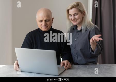 Vista frontale Happy anziani 70s uomo grigio pelato imparare utilizzando il software del computer con cura figlia cresciuta, anziani pensionati e tecnologia moderna Foto Stock