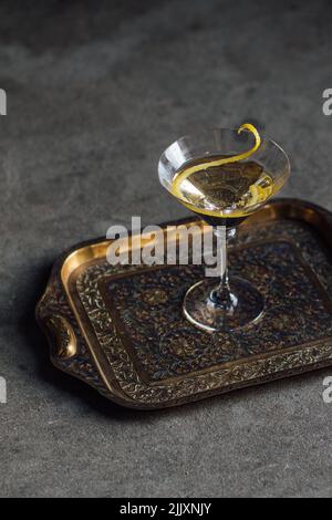 Martini con una lunga torsione al limone su vassoio in ottone su pavimento in cemento Foto Stock