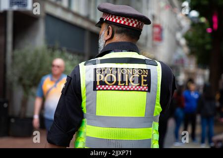 LONDRA, REGNO UNITO - 28 LUGLIO 2022. Una vista posteriore di un poliziotto metropolitano in uniforme e sulla strada con un cartello della polizia della Città di Londra sul retro Foto Stock