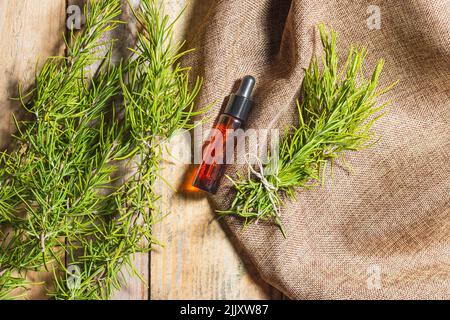 Visto dall'alto, su alcune tavole di legno, c'è una bottiglia di vetro marrone con olio essenziale tappato con un tappo nero con contagocce. Intorno è un sacco Foto Stock