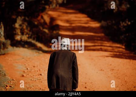 Un vecchio uomo cammina lungo le strade rosse africane. Foto illustrativa della vita in Africa e Kenya. Vita di un pensionato in pensione in Africa orientale Foto Stock