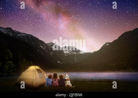 Famiglia campeggio sotto il cielo stellato notte. Visione della Via Lattea. Falò del campo con i bambini. Viaggi ed escursioni con i bambini piccoli e il cane. Foto Stock