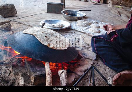 Una donna beduina produce il tradizionale flatbread sulla sommità di un pezzo di metallo convesso e di un fuoco aperto Foto Stock
