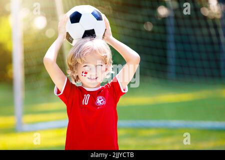 Tifosi di calcio della Danimarca che acclamano. I bambini danesi giocano a calcio e festeggiano la vittoria sul campo all'aperto. Sostenitore del team Danmark. Ragazzino nella bandiera di Dansk Foto Stock