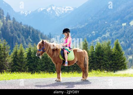 Pony per bambini sulle Alpi. Famiglia primavera vacanza sul ranch cavallo in Austria, Tirolo. I bambini cavalcano i cavalli. Bambino che si prende cura di animali. Foto Stock