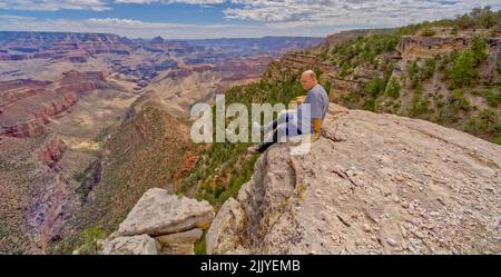 Un uomo seduto su una scogliera al Grand Canyon, Arizona, a ovest di Twin vista si affacciano. Foto Stock