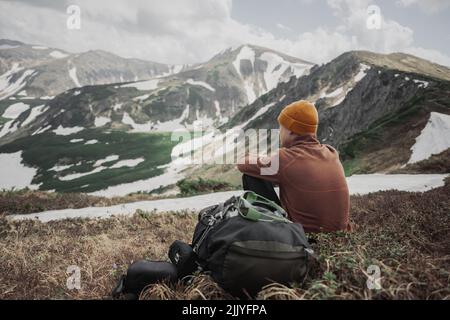 Un turista siede sul bordo di una cima di montagna. Montagne nebbia sullo sfondo. Fotografia di paesaggio Foto Stock