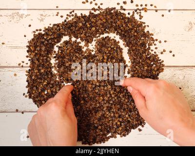 Mano femminile che disegna un simbolo di cuore nel mucchio di buckwheat organico buccia su un fondo di legno assi, usato come riempimento per cuscino di grano saraceno Foto Stock