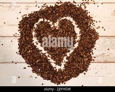 Un simbolo di cuore disegnato nel mucchio di buckwheat organico buccia usato come riempimento per cuscino di grano saraceno su un fondo di legno di assi Foto Stock