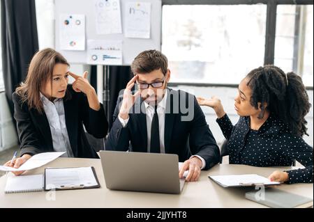 Ambiente di lavoro stressante. I colleghi sono confusi dalle informazioni, in perdita dai risultati del profitto del progetto, sperimentando emozioni negative, parlando al desktop in ufficio Foto Stock