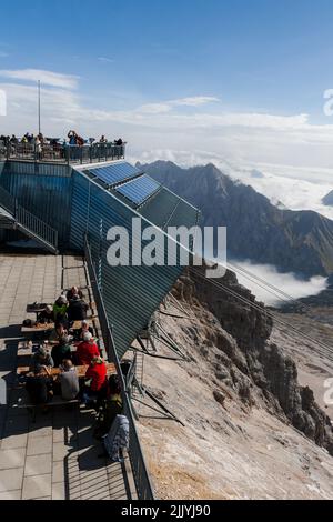 I turisti che pranzano al ristorante sulla cima delle montagne di Zugspitze. Baviera, Germania. Centro di ricerca tecnica. Antenne per telecomunicazioni con radar recei Foto Stock