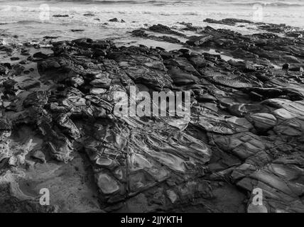 Le onde si lavano dolcemente su formazioni rocciose sulla sabbia - B&W. Foto Stock