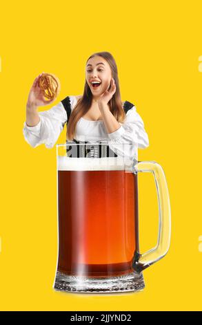 Collage con bella donna in abiti tradizionali tedeschi tenendo pretzel e grande bicchiere di birra su sfondo giallo Foto Stock