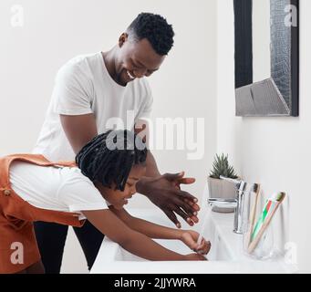 Insegnandole l'importanza dell'igiene, un giovane padre che aiuta sua figlia a lavarsi le mani nel bagno di casa. Foto Stock