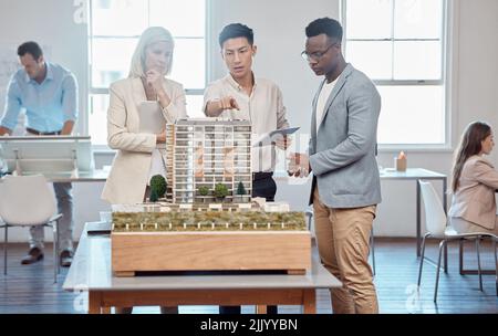 Diversi architetti o project manager discutono del piano di espansione dell'edificio. L'ingegnere asiatico presenta il modello e 3D per un nuovo ufficio a. Foto Stock