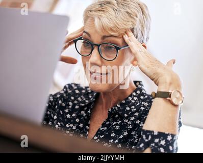 OH, guarda, l'ho fatto di nuovo. Una donna matura seduta da sola e che si sente stressata mentre usa il suo laptop per lavorare da casa. Foto Stock