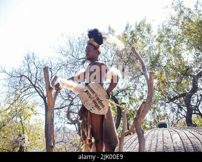 Johannesburg Sud Africa - Agosto 13 2027; Tall African man in piedi tenendo scudo in costume guardando a distanza in attrazione turistica. Foto Stock