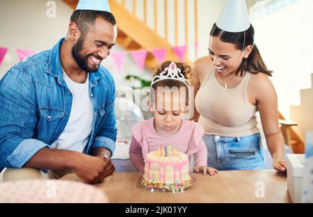 Soffiate fuori le candele. Una bambina festeggia un compleanno con i genitori a casa. Foto Stock
