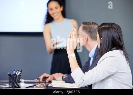 ID piace fare un suggerimento... una giovane donna d'affari che alza la mano durante una riunione in un ufficio. Foto Stock