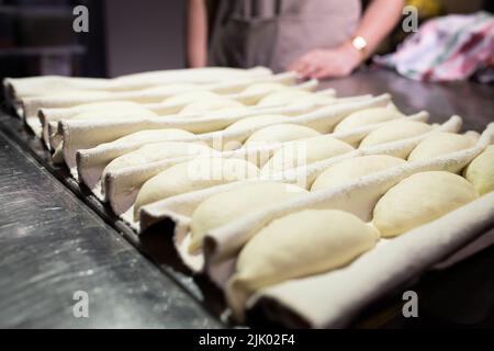 Il panettiere controlla la prova dei panini stampati la Ciriola romana prima della cottura. Vista frontale. Foto Stock