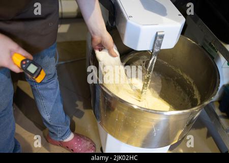 Il panettiere impasta il pane in un impastatore. Il processo di preparazione del pane in una panetteria artigianale. Misurazione della temperatura dell'impasto. Vista frontale. Foto Stock