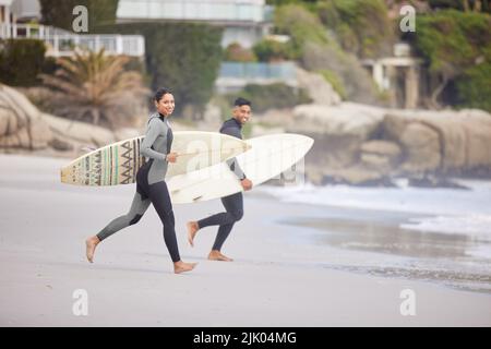 Andiamo a fare surf. Una giovane coppia che corre in acqua con tavole da surf in spiaggia. Foto Stock