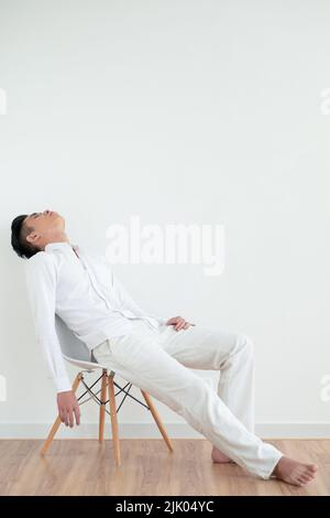 Giovane uomo asiatico stanco che dorme sulla sedia Foto Stock