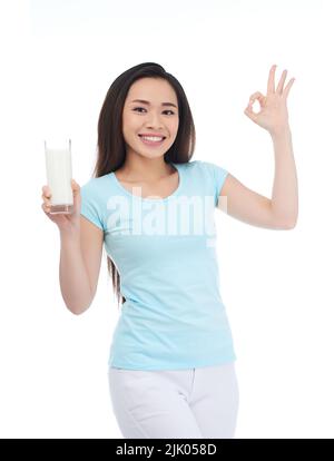 Ritratto di bella donna asiatica che mostra il gesto OK tenendo in mano un bicchiere di latte, isolato su sfondo bianco Foto Stock