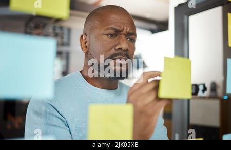 La pianificazione è il preludio a qualsiasi azione di successo. Un uomo d'affari brainstorming con note appiccicose su uno schermo di vetro. Foto Stock