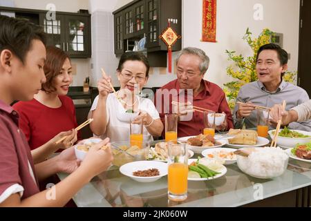 La famiglia mangia vari piatti tradizionali alla festa del Tet. Scorre desiderio di fortuna e ricchezza in background Foto Stock