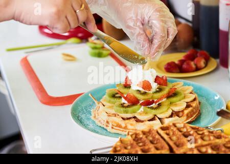 Immagine ravvicinata del panettiere che decora le cialde con frutta e panna montata Foto Stock