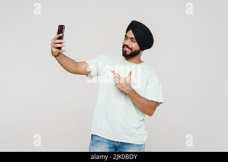 Uomo del sud asiatico prendendo selfie sul cellulare e gesturing isolato su parete bianca Foto Stock