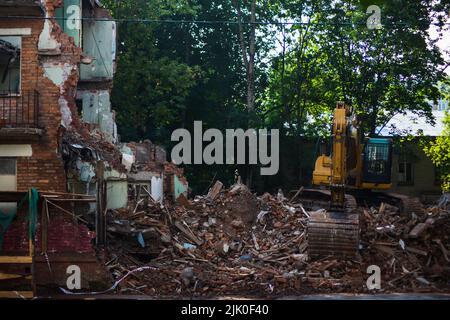 Demolizione di un edificio in mattoni con braccio meccanico dell'escavatore. Distruzione di abitazioni dilatate. Macchine pesanti attrezzature idrauliche da costruzione Foto Stock