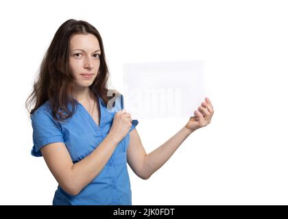 Elegante ragazza snella in abito blu tiene in mano un foglio di carta bianco, coprendo il viso su sfondo bianco. Cartello per scrivere parole a livello di hea Foto Stock