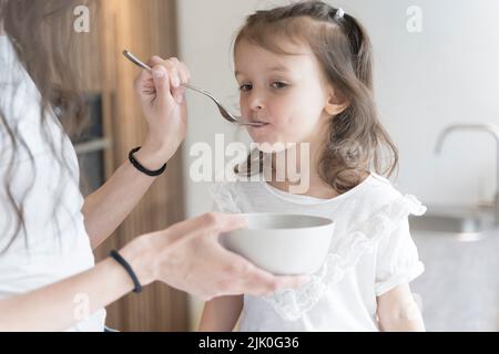 La mamma nutre la colazione della figlia nella cucina casalinga al mattino. Alimenti per bambini, famiglia, concetto di cura. Foto di alta qualità Foto Stock