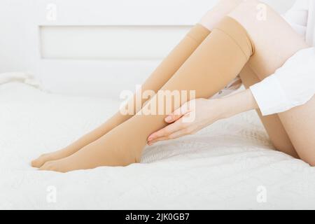 Gambaletti o calzini. Calze a compressione beige su una donna in una stanza bianca. Ragazza che mette su calze a casa. Belle gambe femminili Foto Stock